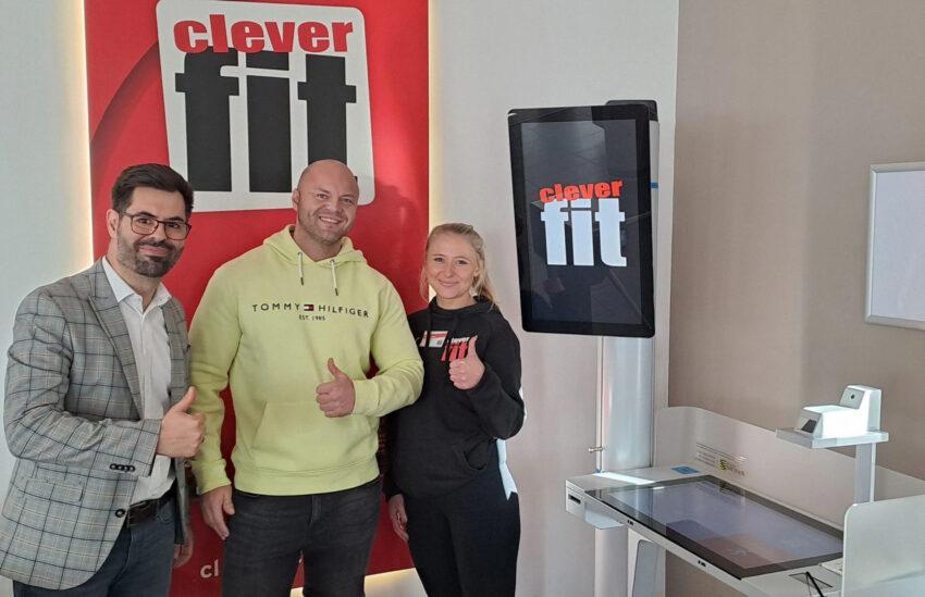 DeGIV Mitarbeiter Roman Wygas links neben 2 Mitarbeitende des Fitnessstudios "cleverfit" Dresden, rechts daneben ein Gesundheitsterminal